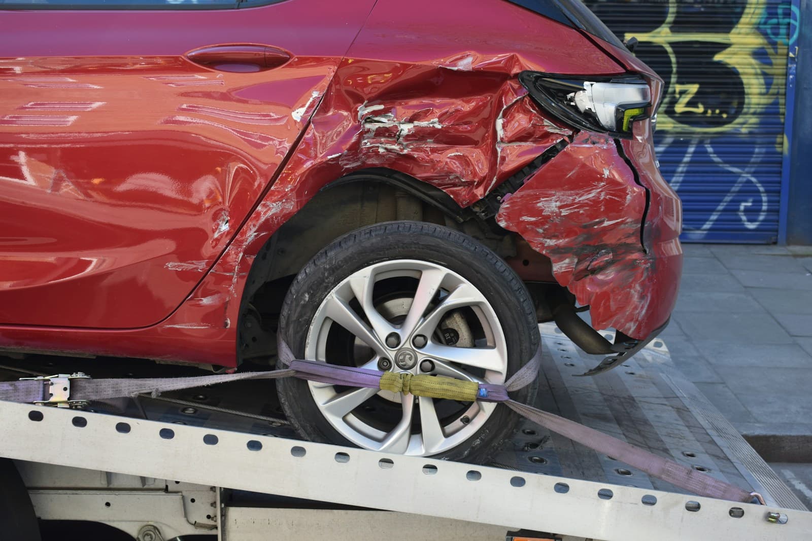 Damaged red car on crash test platform showing impact deformation to front end and wheel area