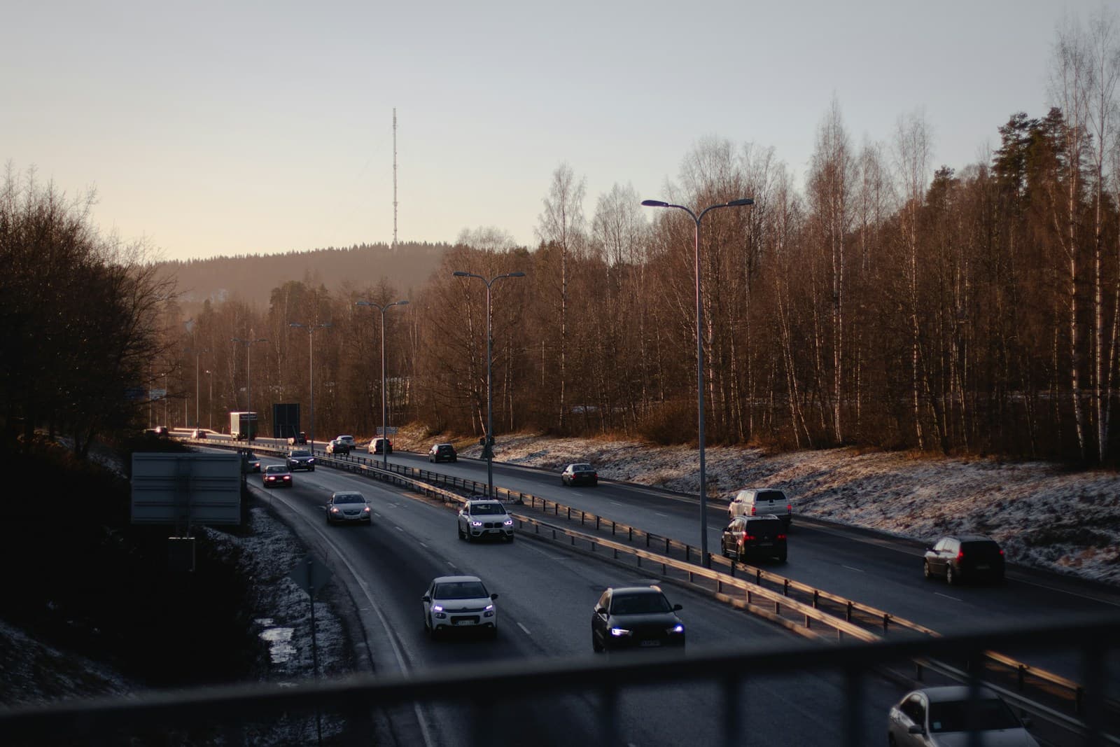Highway with evening traffic flowing in both directions, surrounded by bare trees and hills at dusk